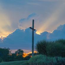 big wooden cross on green grass field under the white clouds